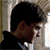 Static 50x50 pixel icon showing a side-profile of a person with dark hair and brown skin wearing a black jacket over a white shirt, set against a light background with vertical lines.