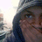 A person wearing a hooded garment with light and dark stripes covers their mouth with one hand while looking slightly upward.
