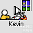 Pixel art of a person in a yellow shirt sitting at a desk with a computer, window with blue and green panes, and text "Kevin" below.