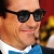 A pixelated close-up of a person wearing dark sunglasses, a white shirt, and blue tie against a red background.