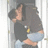 Two figures in a close embrace, one with dark hair and light skin holding another figure wearing a gray top and blue pants.