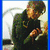 A person in a dark jacket holds an object while standing against a light background with curved lines.