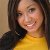 A pixelated close-up of a person with shoulder-length brown hair wearing a yellow top and dark outer garment, smiling at the camera.