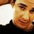 Pixelated close-up of a person's face with light brown hair, wearing dark clothing against a white background.