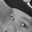 A grayscale close-up of a stylized face with large eyes and smooth shading, cropped to show only the upper portion against a dark background.
