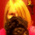 Pixelated static image shows a figure with long blonde hair against red background, wearing dark brown clothing and pink shoulder accents.