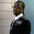 Pixelated static image of a person in formal attire against a two-toned background with visible grid lines.