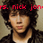 Pixelated image of a person with dark curly hair wearing a dark jacket over a light shirt, with red text partially visible at the top.