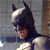 Pixelated profile view of a figure in a dark cowl with pointed ears, light-colored chest armor, and a blurred background with vertical lines.