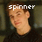 Pixelated image of a person with light skin and brown hair wearing dark clothing, overlaid with white text reading 'spinner' in lowercase letters.