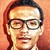 Static pixelated portrait of a person with dark hair, glasses, and light skin tone against warm-toned background.
