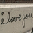 A static pixelated image shows the phrase 'I love you' in dark brown cursive script on a light gray background with subtle horizontal banding.