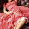 A person in a flowing pink dress with white lace trim, seated with arms crossed and legs bent, against a dark background.