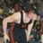 A pixelated image shows a person in a black wrestling singlet with red accents, leaning forward with arms extended, against a blurred crowd background.