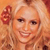 Pixelated close-up of a smiling person with light hair holding a red flower against a warm-toned background.
