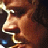 Pixelated close-up of a person's face with brown hair and light skin tone, featuring visible facial features like eyes, nose, mouth, and ear against dark background.