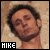 A static image of a person with dark hair and stubble against a textured beige background, labeled 'HIKE' in the bottom-left corner.