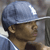 Pixelated close-up of a person wearing a light blue cap with a white brim, brown skin, and a light blue shirt with white trim.