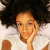 A person with dark curly hair wears a white shirt and rests their hand on their cheek in a static pixelated image.