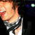 Pixelated close-up of a person with light skin and brown hair wearing a dark jacket over a white shirt, set against a black background with blue and green lights.