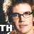 Static 48x48 pixel icon showing a close-up of a person's face with glasses and light brown hair, overlaid with large white text "TH" in the bottom-left corner against a dark background.
