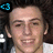 A pixelated close-up of a person's face with dark hair, wearing a white shirt and holding a microphone against a dark background.