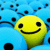 Static pixelated icon featuring a yellow smiley face with black eyes and mouth against a blue background with scattered black dots.