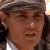 A pixelated close-up of a person wearing a dark cap and dark clothing with a light-colored collar, set against a blurred background.