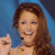 A pixelated image of a person with long brown hair smiling and holding up a small object against a blue background.