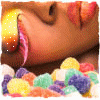 A close-up of a cartoon character's face with a pink tongue sticking out, surrounded by colorful round candies, with a yellow and orange gradient background.