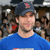 Pixelated image of a person in blue shirt with dark hair, surrounded by blurred background figures.