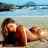 Pixelated static image of two people lying on a beach with blue sky background, one person in dark clothing, the other in light-colored clothing, both facing left.