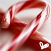 A close-up of a red and white striped candy cane with a glossy surface, featuring a small white heart-shaped icon in the bottom right corner.