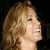 Pixelated close-up of a person with light brown curly hair, smiling with eyes closed against a dark background.