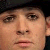 A pixelated close-up of a person's face showing eyes, nose, mouth, and part of a dark cap, with visible skin tones and a neutral expression.
