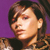 Pixelated close-up of a person with dark hair against a solid purple background, wearing a dark top with a patterned collar.