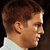 Pixelated profile view of a person with short brown hair wearing a light-colored collared shirt against a dark background.
