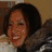 A pixelated image of a person with long dark hair smiling, wearing a dark jacket with fur trim and light-colored clothing underneath.