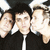 A 50x50 pixel animated buddy icon featuring a contact sheet of two frames showing three people in black jackets with white collars, next to green text reading "GREEN DAY" on a dark background.