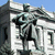 A pixelated image of a building with columns and a statue on top, set against a blue sky.