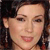 A pixelated close-up of a person's face with dark hair, visible ear, and light skin tone, showing a slight smile.