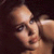 Pixelated close-up of a person's face with light skin tone, dark hair visible at top right, and neutral expression against dark background.