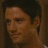Pixelated close-up of a person's face with dark hair, neutral expression, and brown skin tone against a dark background.