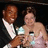 Two pixelated figures in formal attire, one holding a trophy above their head against a dark background.