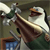 A pixelated image shows a white bird with brown accents perched on a branch, holding a green object in its beak against a muted green background.
