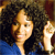 Pixelated image of a person with curly dark hair wearing a blue top, holding a light-colored object near their face.