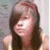 A person with long dark hair and bangs wears a light-colored sleeveless top against a blurred background.