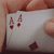 A hand holds a white playing card with red spade symbols; two spades are visible near the top left, one near the bottom center.