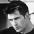 Black-and-white pixelated static image of a person's face with dark hair, visible facial features including eyes and nose, and partial shoulder in low-resolution 50x50 icon format.