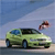 A light green sedan with dark windows and black wheels is positioned on a road under a blue sky, with a small blurred object in the upper right.